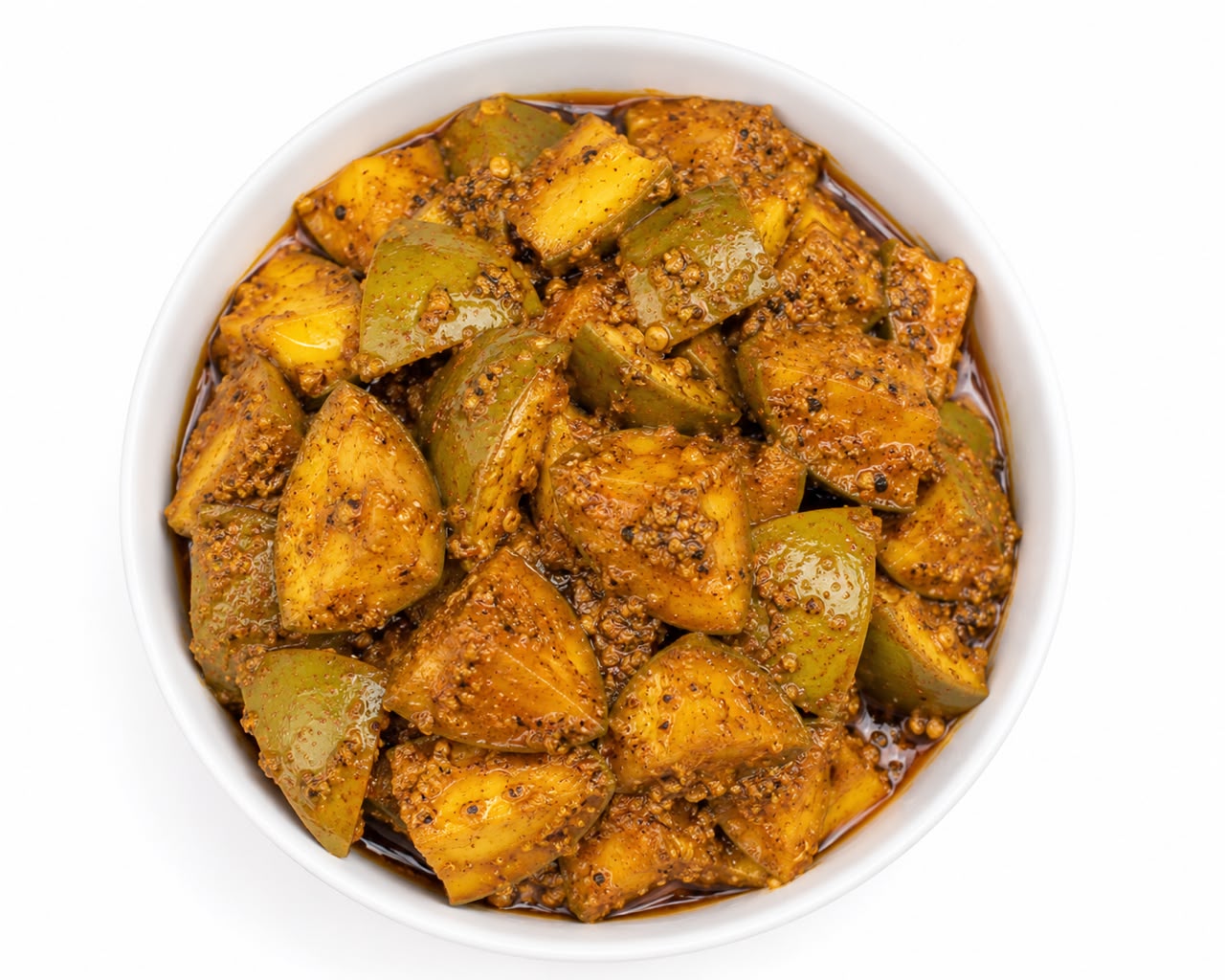 A top-down view of a white bowl filled with a chunky, spiced mango pickles, in a brown spice mixture with visible mustard seeds, on a white background.