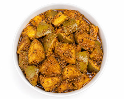 A top-down view of a white bowl filled with a chunky, spiced mango pickles, in a brown spice mixture with visible mustard seeds, on a white background.