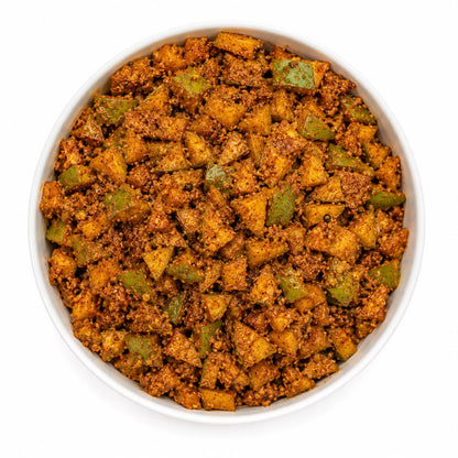A top-down view of a white bowl filled with a textured, spiced food mixture containing diced yellow-orange vegetables and green pieces, isolated on a white background.