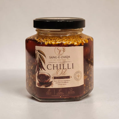 A glass jar of Sang-e-Zaiqa premium garlic chilli oil, homemade condiment Oil with a black lid and a cream-colored label, set against a plain light gray background.