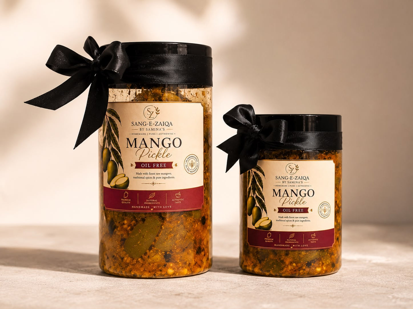 Two glass jars of Sang E-Zarda Mango Pickle, one large and one small, both with black lids and black ribbon bows, set against a warm beige background with soft shadows.